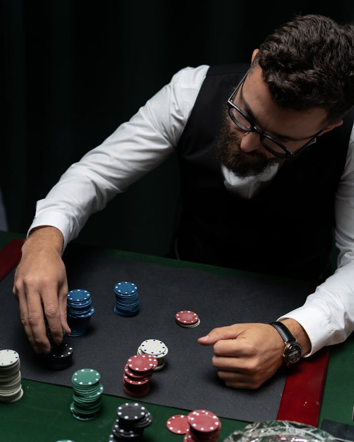 Dubibet Online Gambling Entry | Official Login & Register Page. Bearded man in vest stacking poker chips at a casino table from above, focused and strategic.