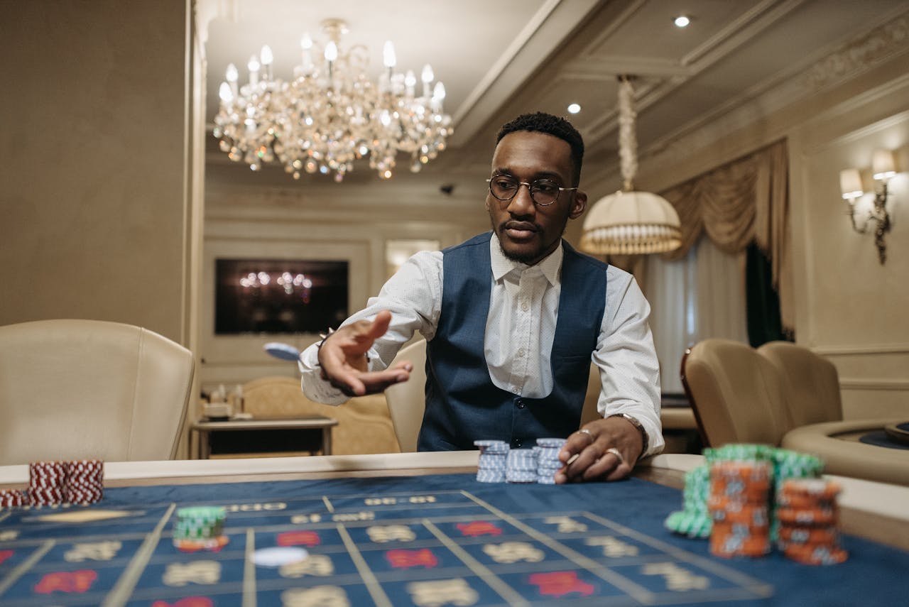 Dubibet Online Casino Access | Easy Login for Real Money Play A man in formal attire plays roulette in a luxurious casino under a chandelier.